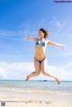 A woman in a blue bikini jumping in the air on a beach.