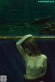 A naked woman sitting on a bench in front of an aquarium.